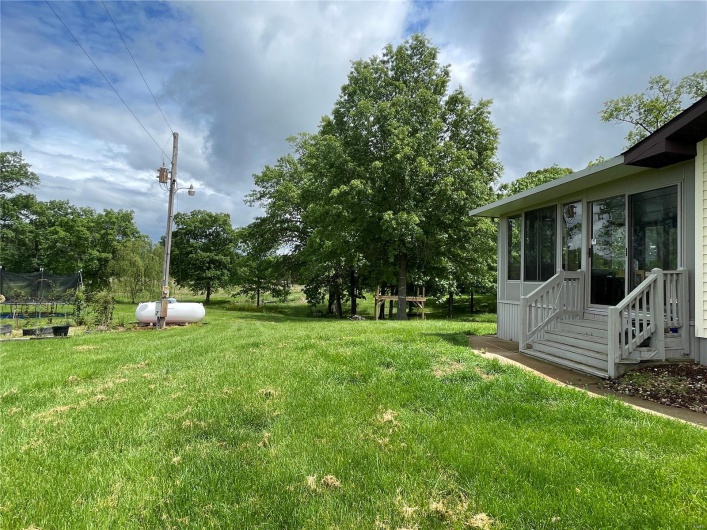 View of grassy yard with a trampoline, a sunroom, and entry steps