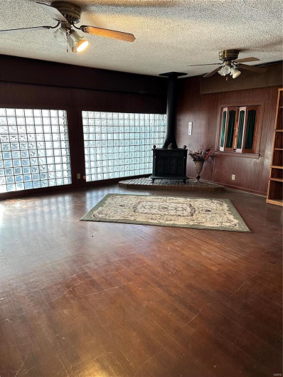 Unfurnished living room with dark wood-type flooring, a wood stove, a textured ceiling, and wooden walls