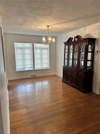 Unfurnished dining area featuring a notable chandelier, a textured ceiling, and hardwood / wood-style floors