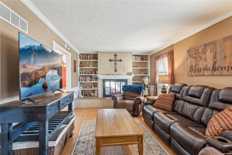 Living room featuring built in features, crown molding, light hardwood / wood-style floors, and a double sided fireplace!
