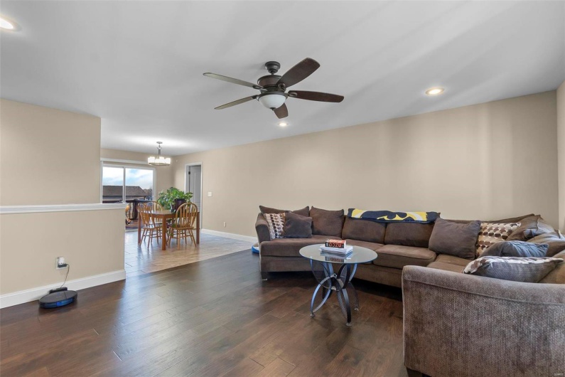 Living room with ceiling fan with notable chandelier and dark wood-type flooring