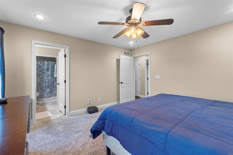 Bedroom with ensuite bathroom, light colored carpet, and ceiling fan