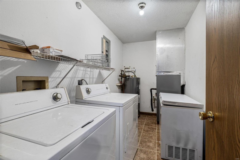 Laundry room with dark tile patterned flooring, washer and clothes dryer, electric water heater, and a textured ceiling