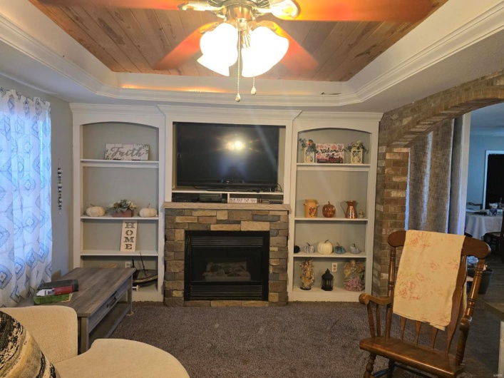 Living room featuring built in shelves, a fireplace, a raised ceiling, and dark colored carpet