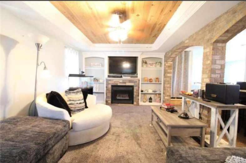 Carpeted living room with a fireplace, a raised ceiling, built in features, and wooden ceiling