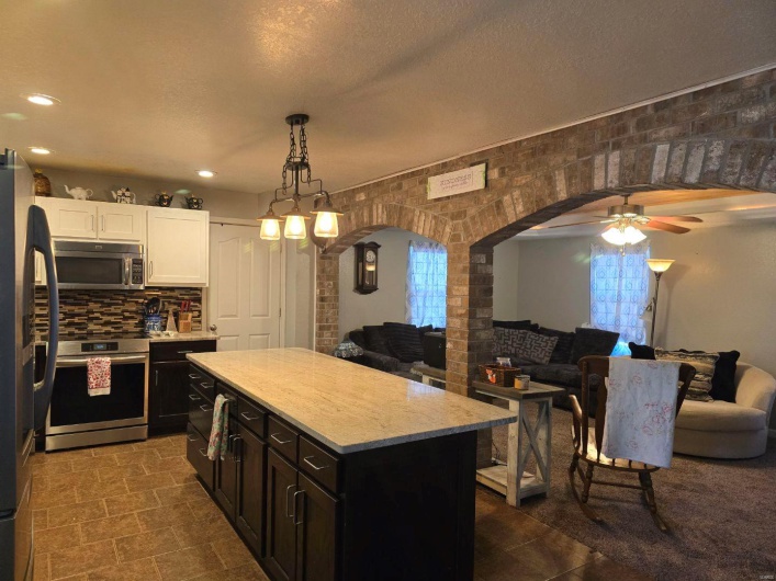 Kitchen with a kitchen island, appliances with stainless steel finishes, white cabinetry, hanging light fixtures, and a textured ceiling