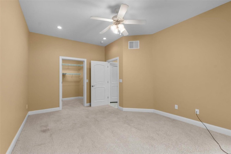 Unfurnished bedroom with light carpet, a walk in closet, a closet, and ceiling fan