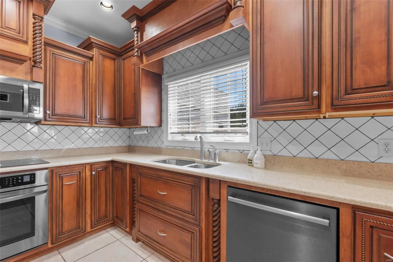 Kitchen featuring light tile patterned flooring, sink, backsplash, ornamental molding, and stainless steel appliances