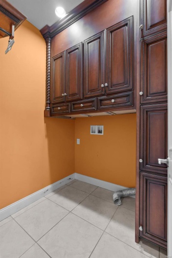 Clothes washing area featuring washer hookup, light tile patterned floors, ornamental molding, and cabinets