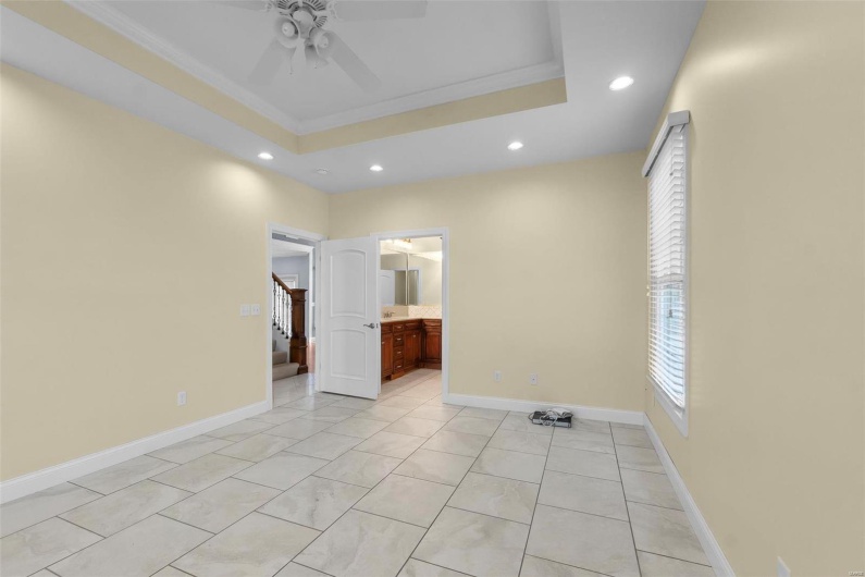 Unfurnished bedroom featuring ensuite bathroom, ornamental molding, light tile patterned floors, ceiling fan, and a raised ceiling