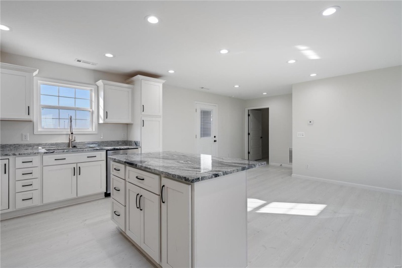 Kitchen featuring a kitchen island, sink, white cabinets, light stone countertops, and light wood-type flooring