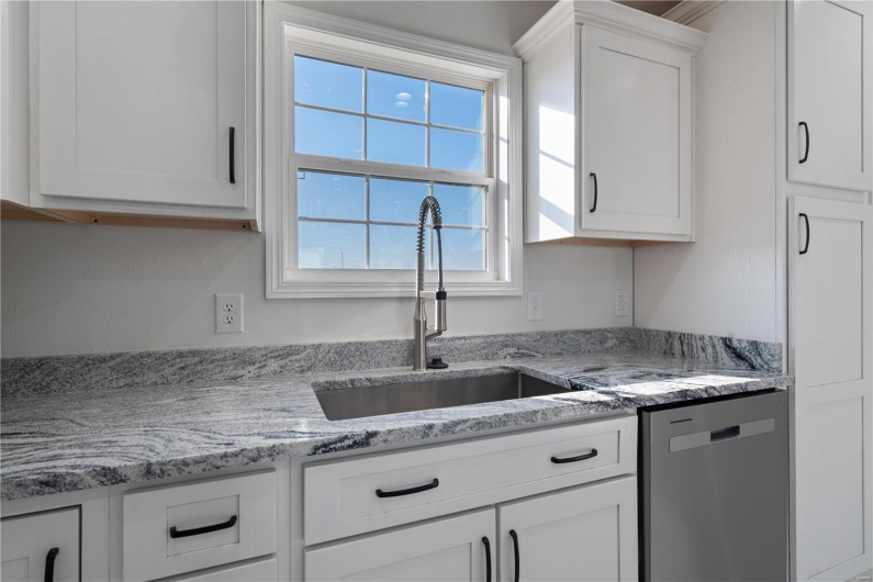 Kitchen with white cabinetry, dishwasher, sink, and light stone countertops