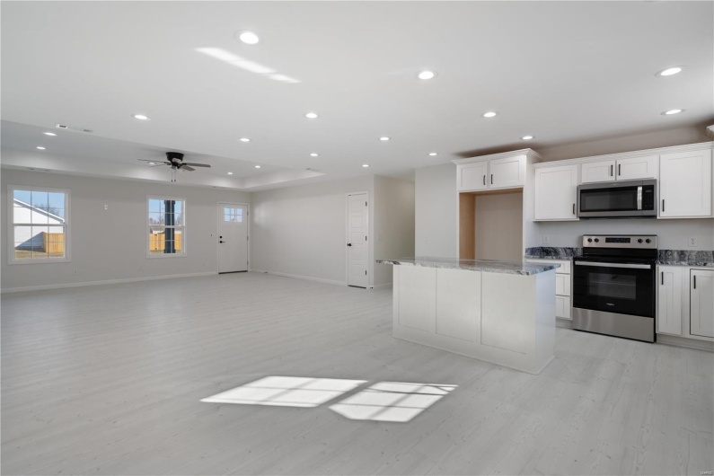 Kitchen with ceiling fan, white cabinetry, stainless steel appliances, a center island, and light stone counters