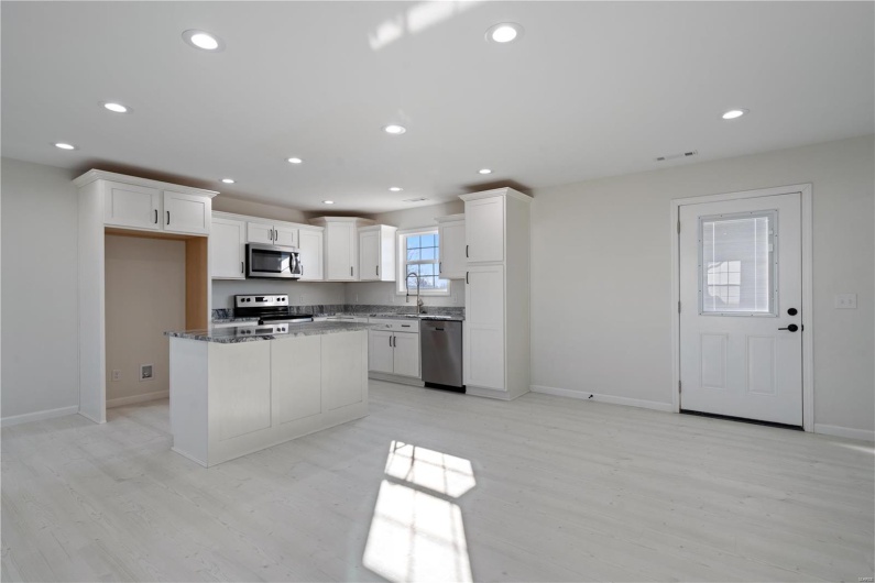 Kitchen with appliances with stainless steel finishes, sink, white cabinets, dark stone counters, and a center island