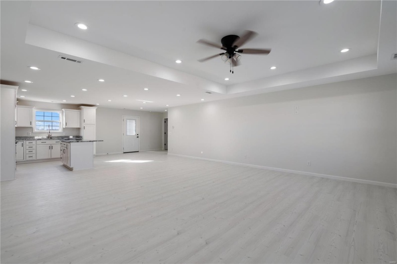 Unfurnished living room with ceiling fan, a tray ceiling, sink, and light wood-type flooring