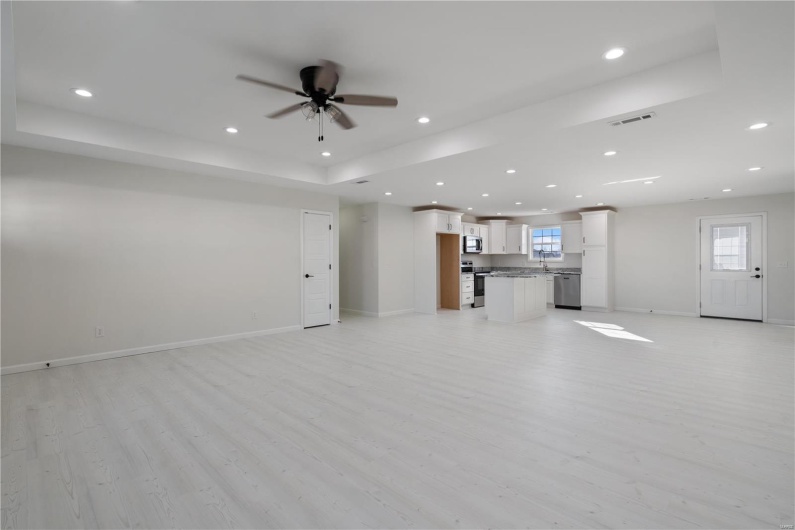 Unfurnished living room with a tray ceiling, ceiling fan, and light wood-type flooring