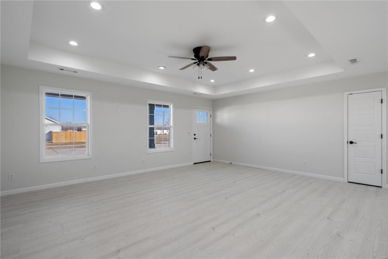 Empty room featuring ceiling fan, light wood-type flooring, and a tray ceiling
