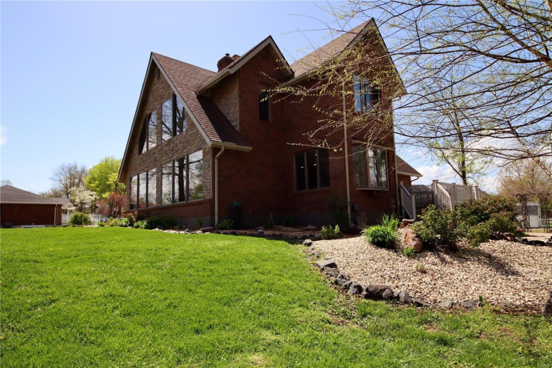 View of side of property with a shingled roof, a chimney, brick siding, and a yard