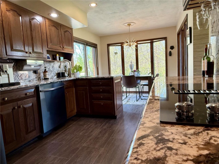 Kitchen with a chandelier, dark wood finished floors, backsplash, stainless steel dishwasher, and light stone counters