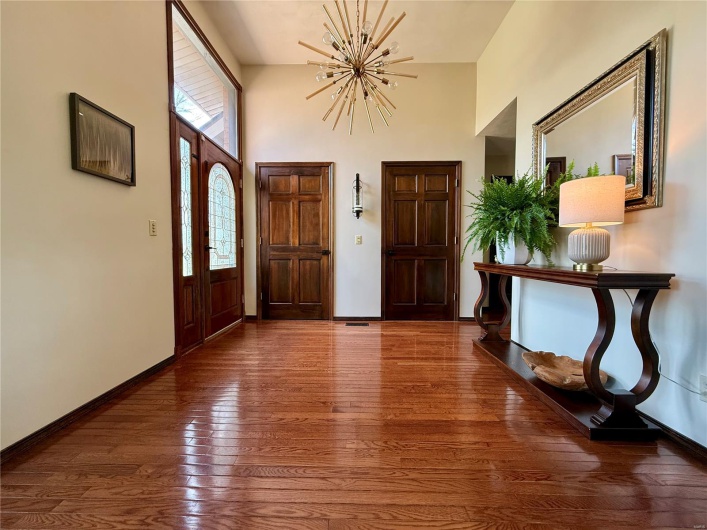 Entryway featuring a towering ceiling, a notable chandelier, baseboards, and hardwood / wood-style flooring