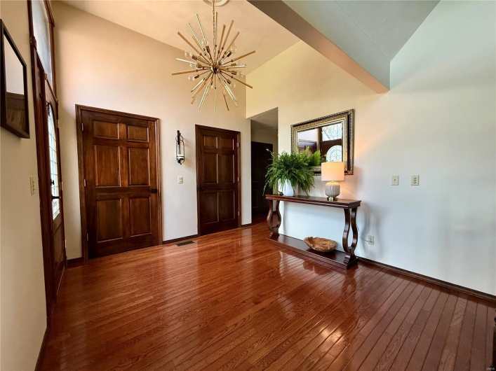 Foyer entrance featuring baseboards, high vaulted ceiling, a chandelier, and hardwood / wood-style flooring