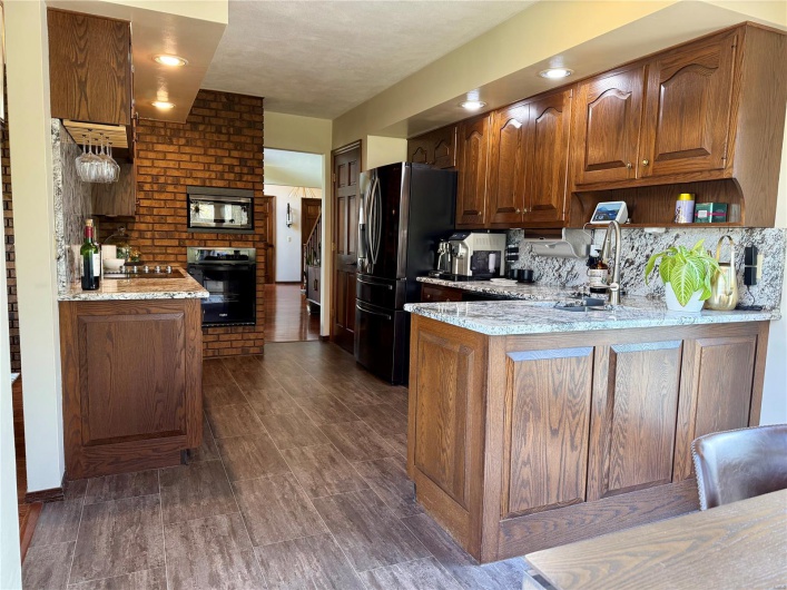 Kitchen with light stone countertops, brown cabinetry, a peninsula, tasteful backsplash, and black appliances