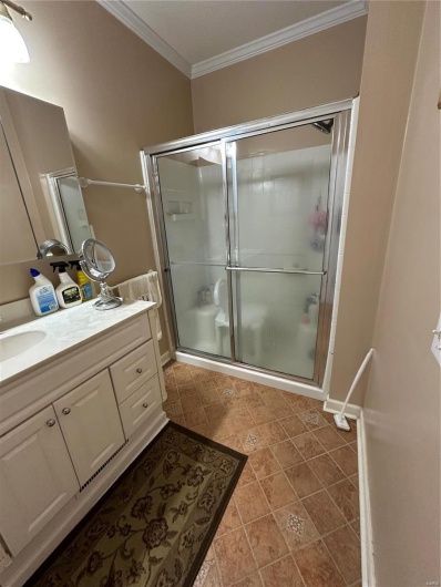 Bathroom with vanity, tile patterned flooring, a shower with shower door, and ornamental molding