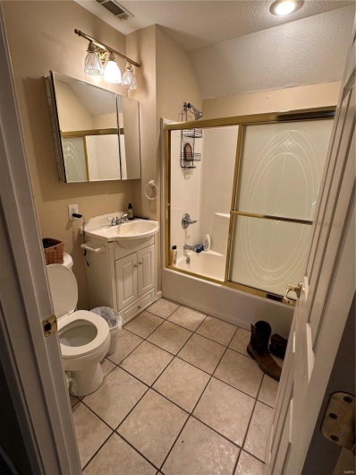 Full bathroom with lofted ceiling, toilet, tile patterned floors, shower / bath combination with glass door, and vanity