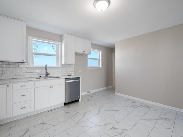Kitchen with sink, white cabinets, backsplash, stainless steel dishwasher, and light stone counters