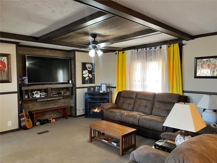 Carpeted living room featuring ceiling fan, beam ceiling, and a textured ceiling