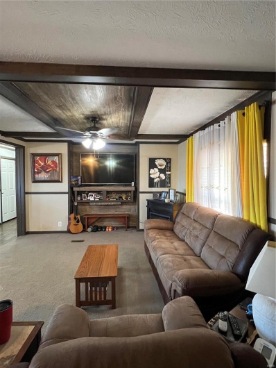 Carpeted living room with beamed ceiling, ceiling fan, and a textured ceiling