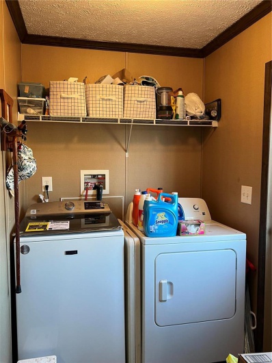 Laundry room featuring crown molding, washing machine and clothes dryer, and a textured ceiling