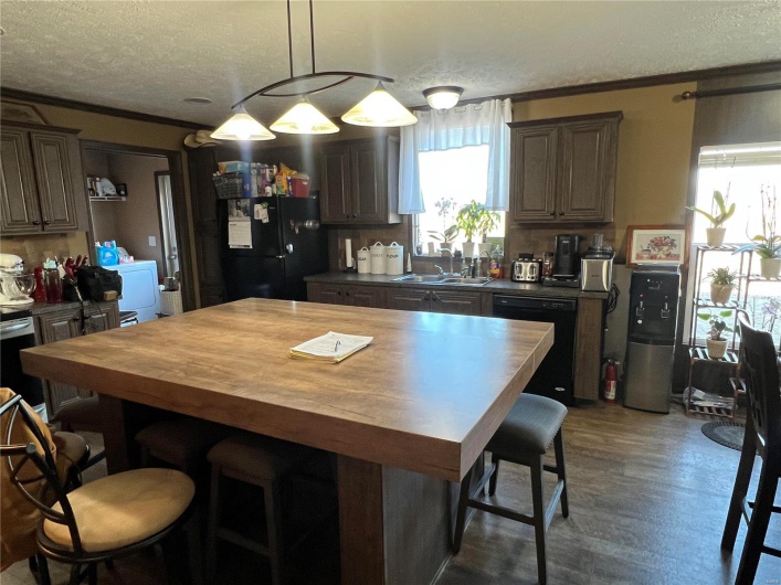 Kitchen featuring pendant lighting, sink, black appliances, a textured ceiling, and a kitchen island