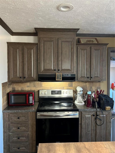 Kitchen with crown molding, dark brown cabinetry, exhaust hood, and stove