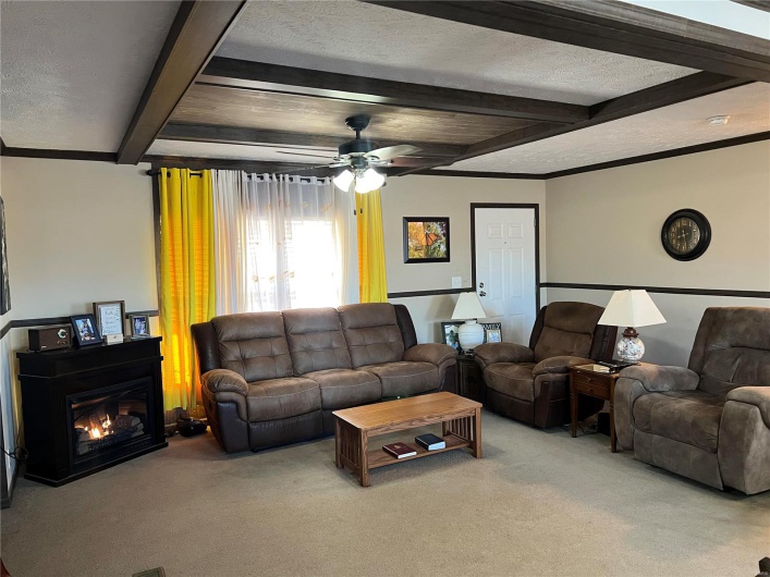 Living room with beamed ceiling, ceiling fan, carpet flooring, and a textured ceiling