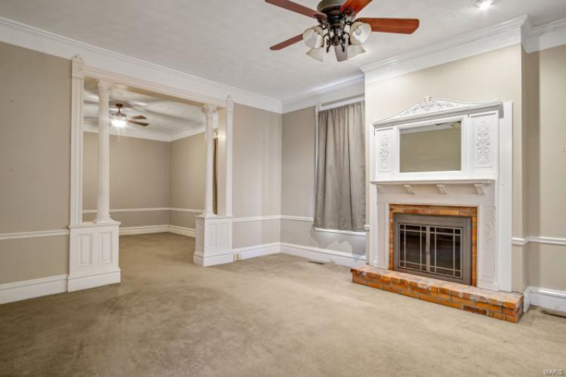 Unfurnished living room with crown molding, carpet floors, ceiling fan, a fireplace, and decorative columns