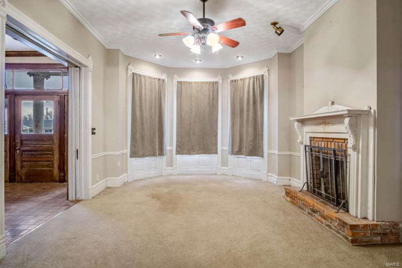 Unfurnished living room with a brick fireplace, crown molding, carpet floors, and ceiling fan