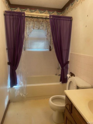 Full bathroom featuring shower / tub combo with curtain, tile walls, vanity, toilet, and a textured ceiling