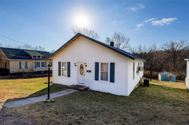View of front facade featuring cooling unit, a shed, and a front yard