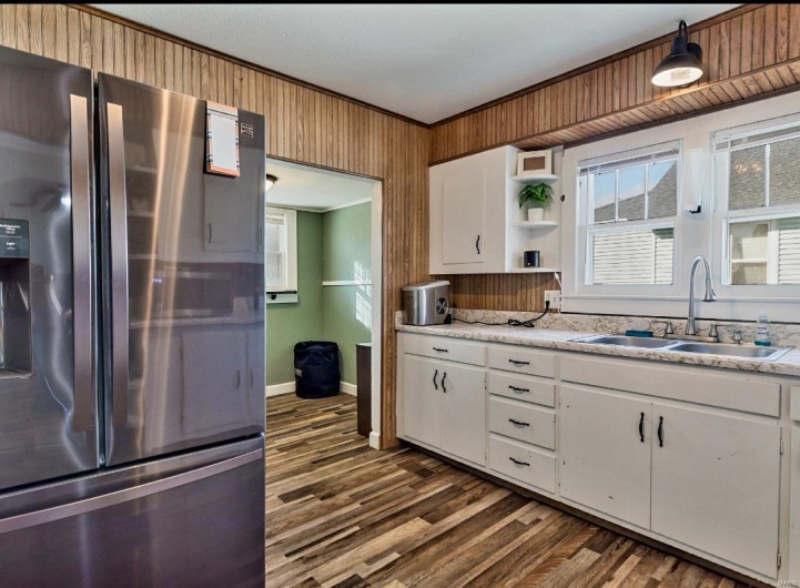 Kitchen featuring stainless steel refrigerator with ice dispenser, dark hardwood / wood-style flooring, ornamental molding, sink, and white cabinetry