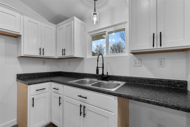 Kitchen featuring a sink, white cabinets, vaulted ceiling, dark countertops, and decorative light fixtures