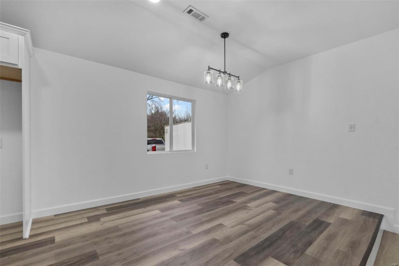 Unfurnished dining area with vaulted ceiling, wood finished floors, visible vents, and baseboards