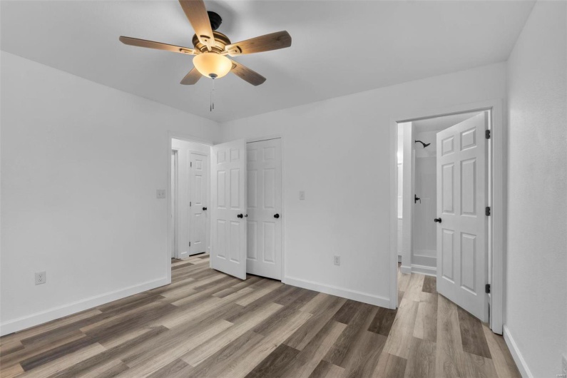 Unfurnished bedroom with ensuite bathroom, ceiling fan, wood finished floors, and baseboards