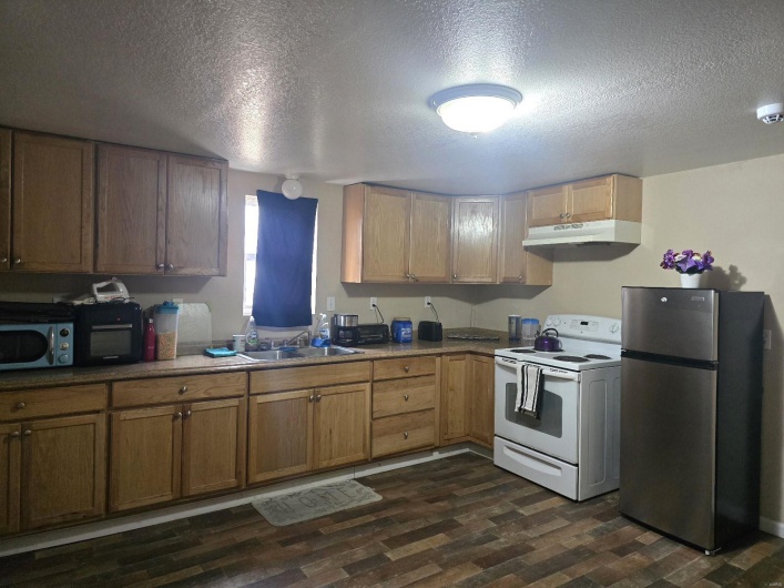 Kitchen with sink, a textured ceiling, dark hardwood / wood-style floors, white electric stove, and stainless steel fridge