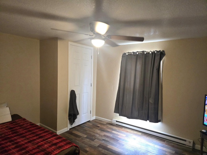 Unfurnished bedroom featuring a baseboard radiator, ceiling fan, a textured ceiling, and dark hardwood / wood-style flooring