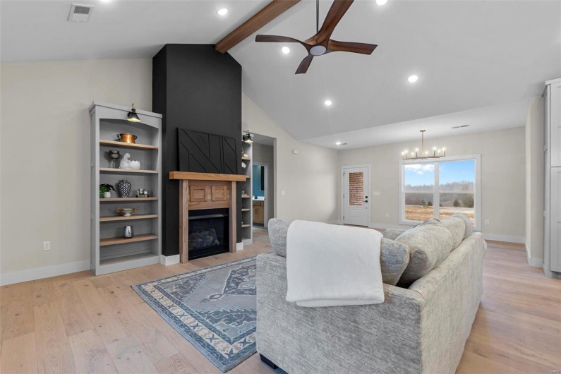 Living room with high vaulted ceiling, a large fireplace, ceiling fan with notable chandelier, beamed ceiling, and light wood-type flooring