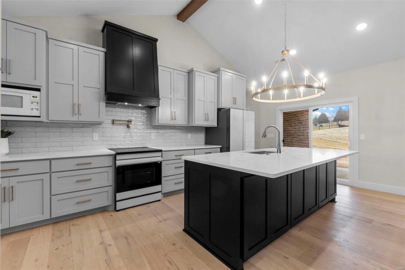 Kitchen with white microwave, refrigerator, an island with sink, sink, and electric stove