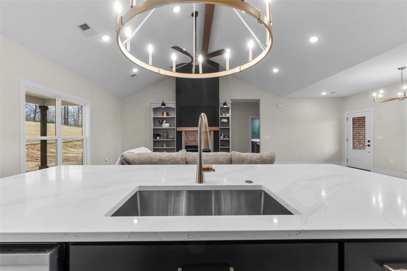 Kitchen featuring lofted ceiling, pendant lighting, sink, a notable chandelier, and light stone countertops
