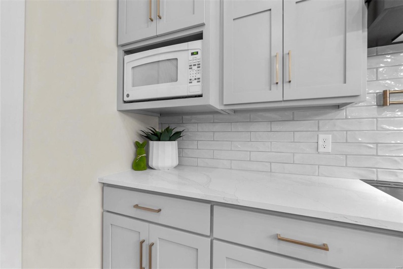 Kitchen featuring light stone counters, backsplash, and gray cabinets