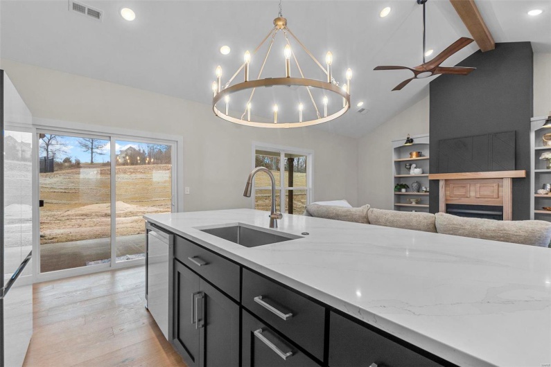 Kitchen featuring dishwasher, sink, hanging light fixtures, light stone countertops, and light wood-type flooring